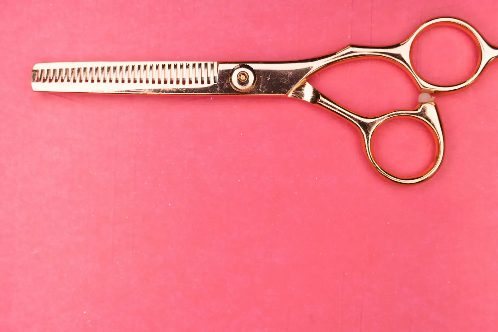 Rose-gold hair shears on a pink background